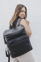 A woman carrying a black leather baby bag backpack