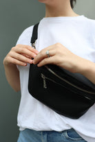 A woman dressed in a white shirt and jeans carries a black bum bag