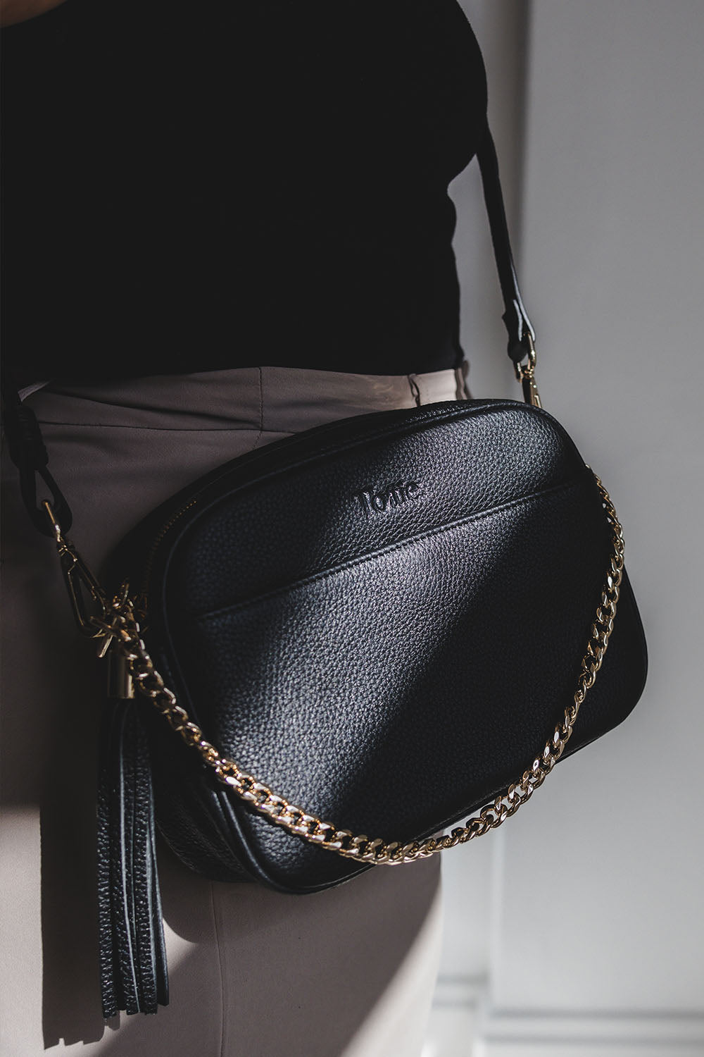 Woman Wearing Black Leather Crossbody Bag with Gold Chain Strap and Tassel from Tottie