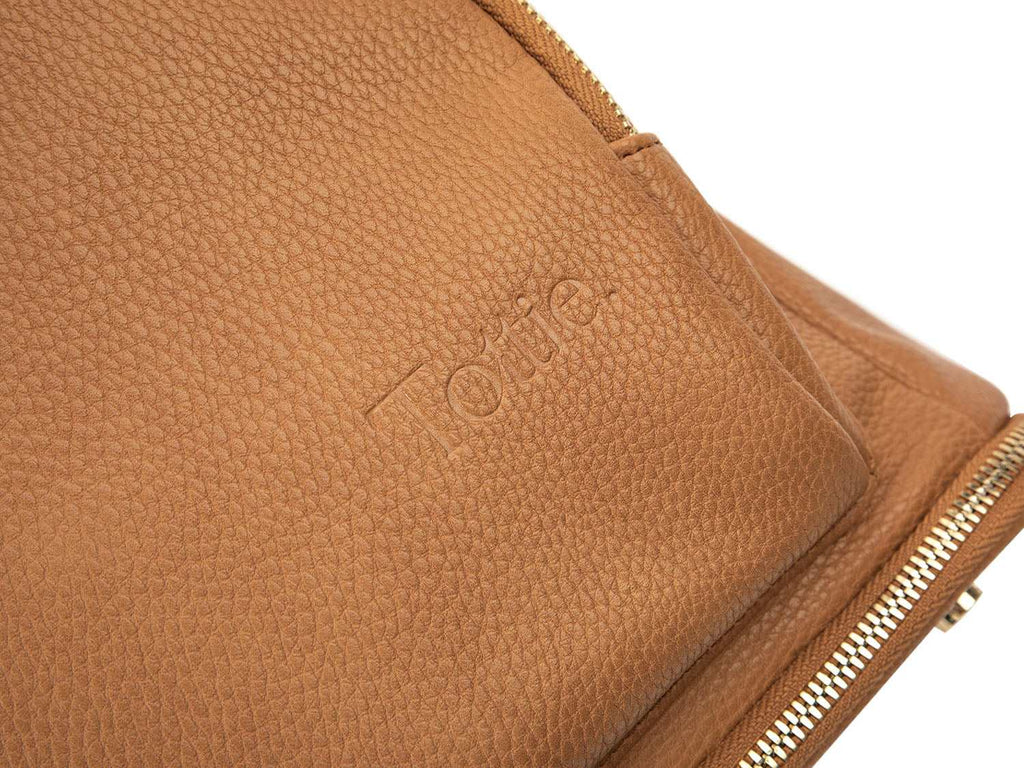 A tan leather baby backpack with gold zippers with Tottie marking on it