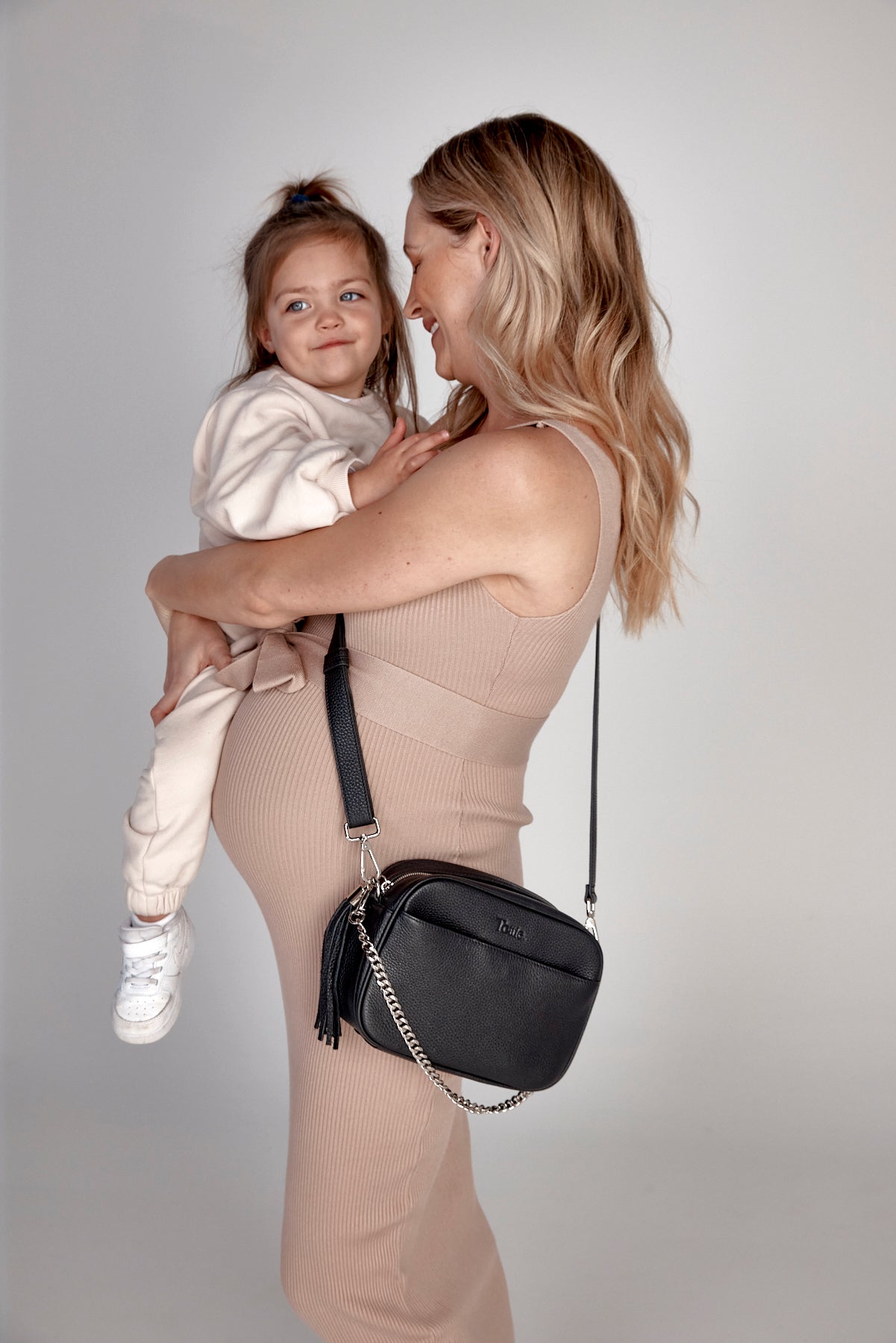 A woman hugging her baby while holding a black Bestie Crossbody Bag from Tottie