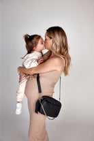 A woman kisses her baby while carrying a black Bestie Crossbody Bag from Tottie