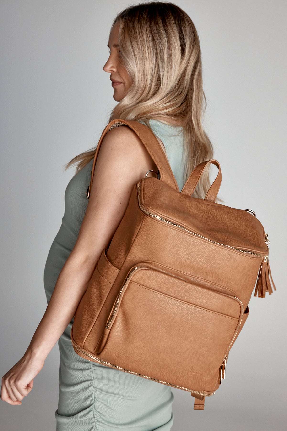 A pregnant woman wearing a tan leather baby backpack