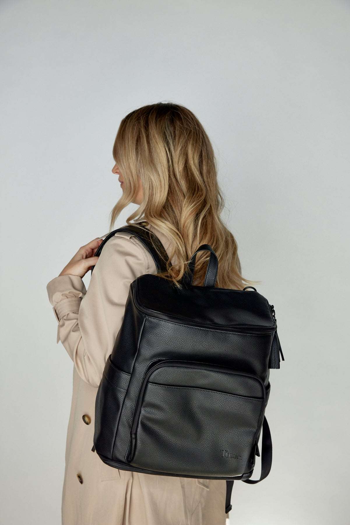 A woman carrying a black leather baby bag backpack