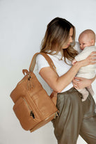 A woman carrying a baby and a tan colour leather baby backpack