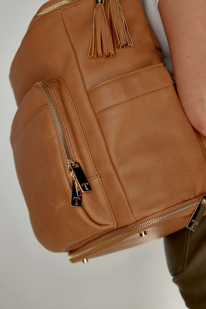 a woman carrying a tan leather baby backpack