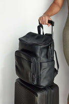 Black leather nappy backpack resting on top of a black luggage