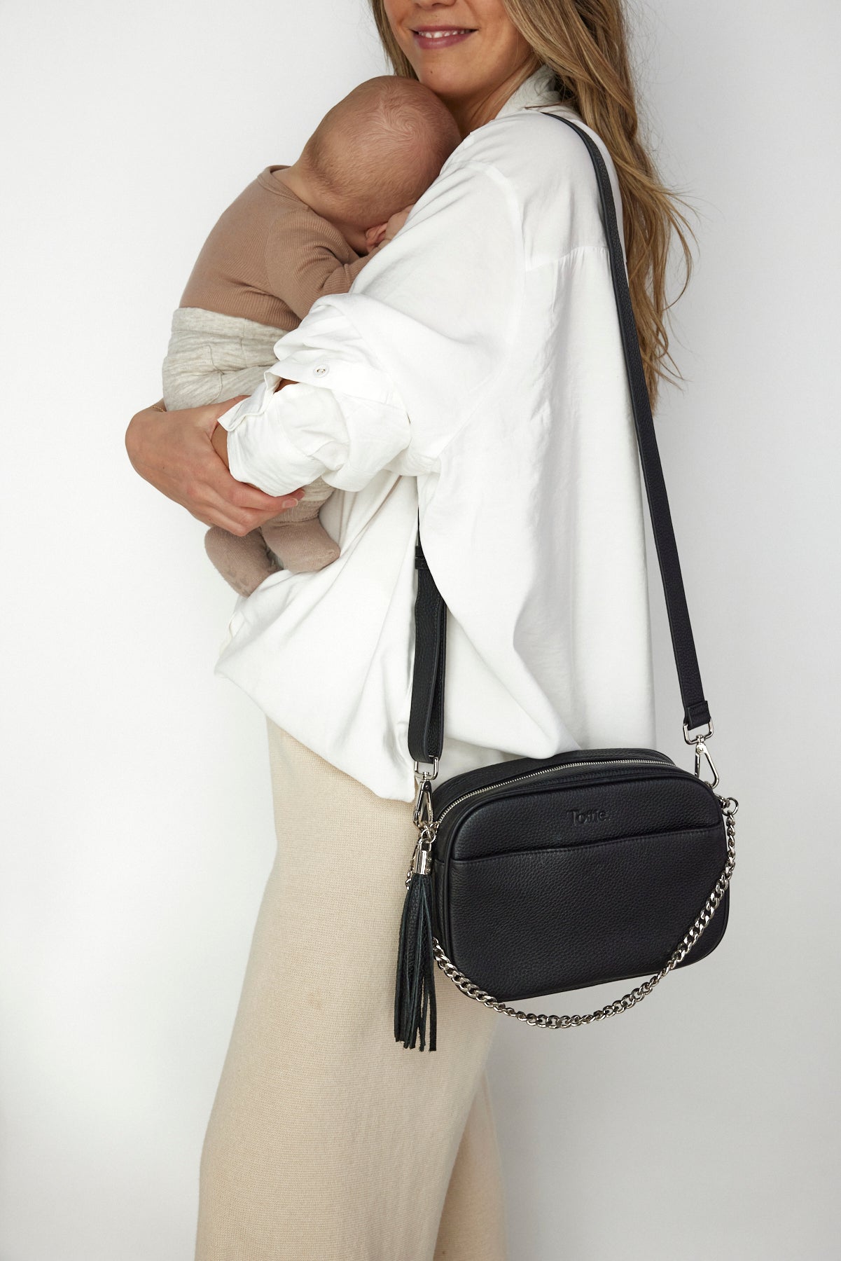 A woman holding her baby while holding a Bestie Crossbody Bag from Tottie