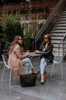 two women sitting and chatting outdoor with a black leather tote bag