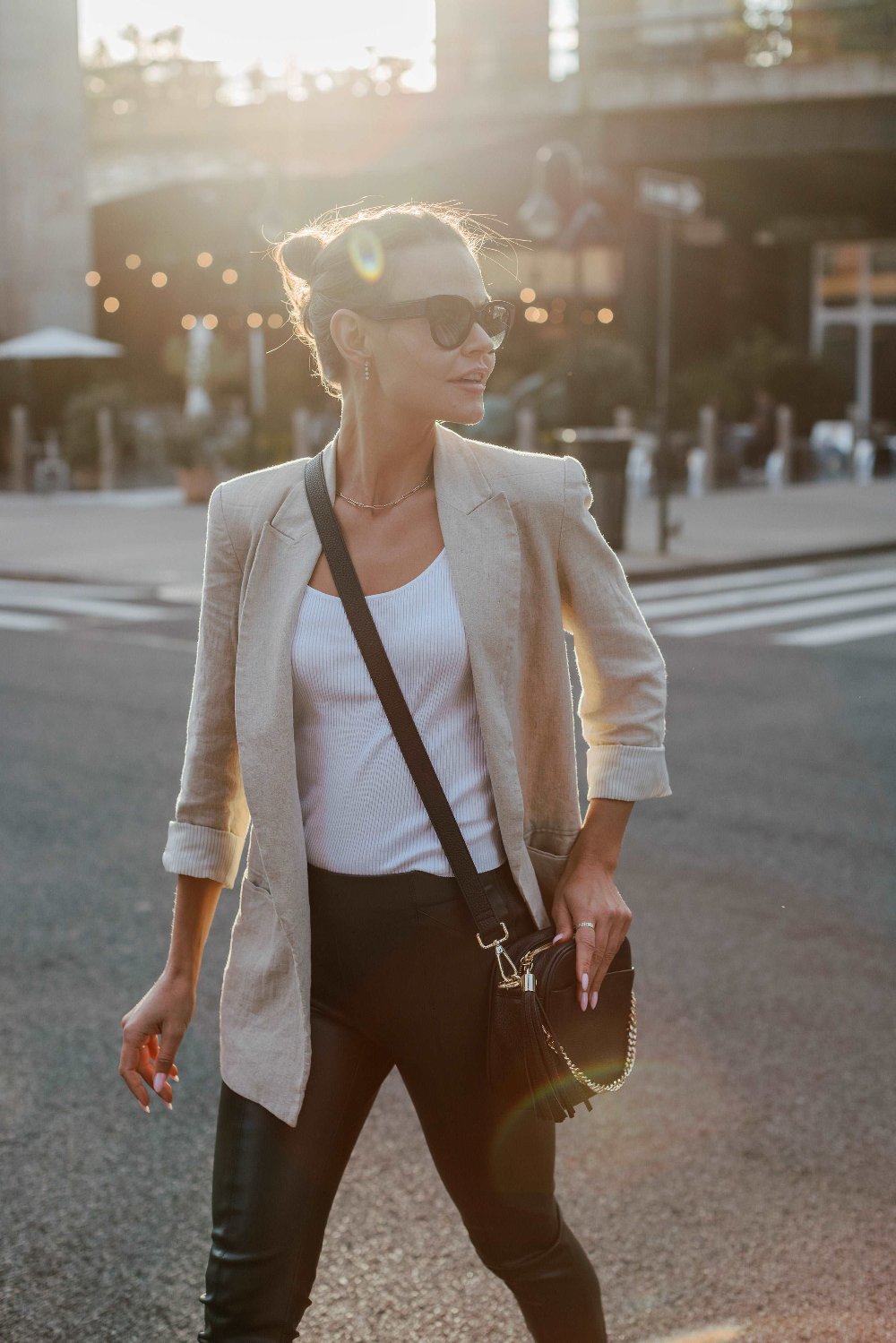 A woman in sunglasses and a blazer walks down the street, carrying a black Bestie Crossbody Bag from Tottie