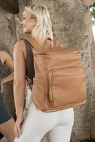 Woman in hiking attire facing away from the camera, carrying a tan nappy bag with gold hardware from Tottie.